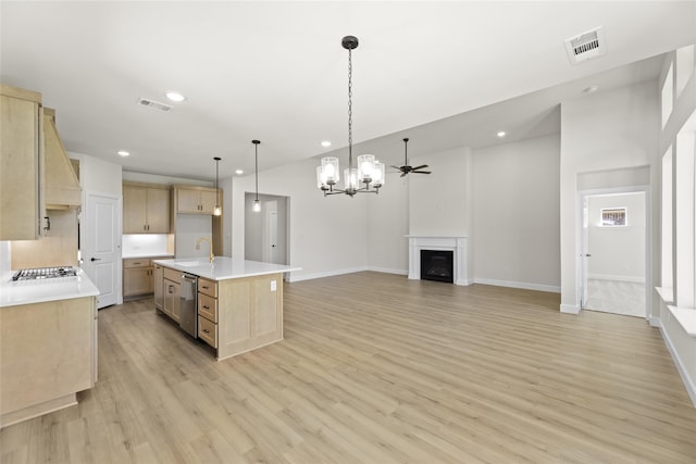 kitchen with light wood-type flooring, light brown cabinets, hanging light fixtures, sink, and an island with sink