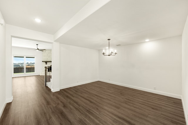 unfurnished room with ceiling fan with notable chandelier, dark hardwood / wood-style floors, and a stone fireplace