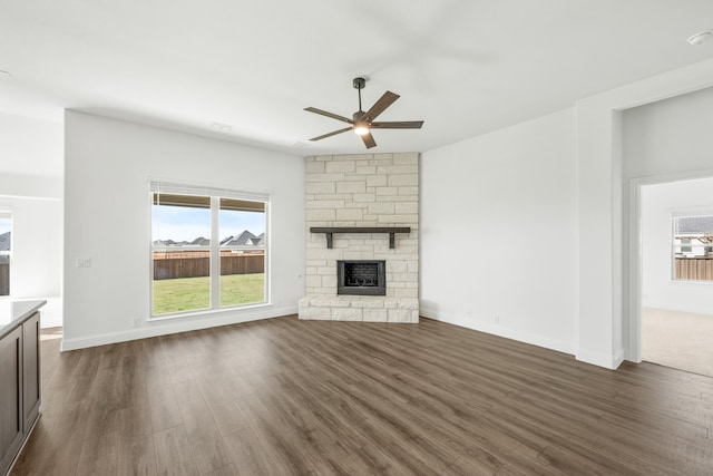 unfurnished living room with a stone fireplace, ceiling fan, and dark hardwood / wood-style floors