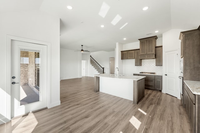 kitchen featuring sink, a kitchen island with sink, wood-type flooring, vaulted ceiling, and decorative backsplash