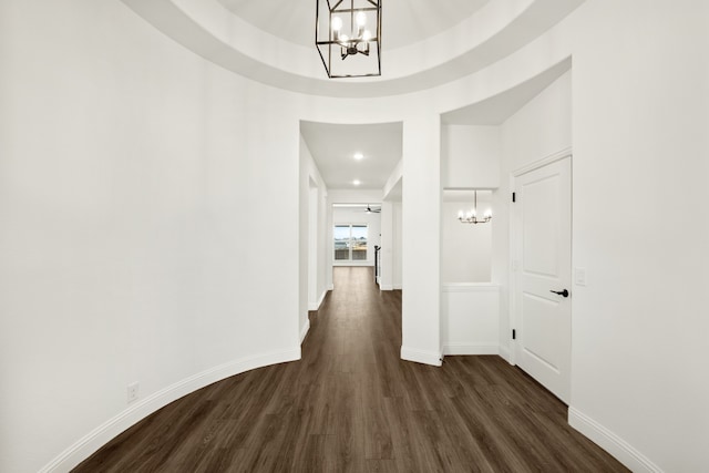 hallway featuring a raised ceiling, dark wood-type flooring, and a notable chandelier