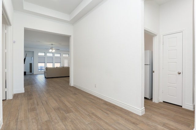 interior space featuring ceiling fan, light wood-type flooring, and a tray ceiling