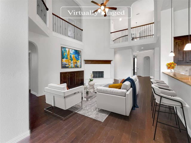 living room featuring a towering ceiling, ceiling fan, and dark wood-type flooring