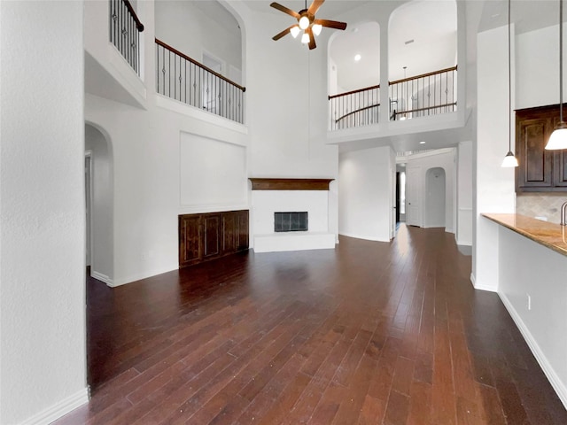 unfurnished living room featuring a high ceiling, ceiling fan, and dark wood-type flooring