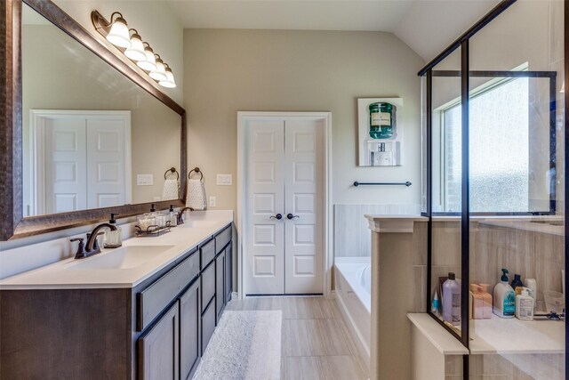 bathroom featuring tile flooring, plus walk in shower, vanity with extensive cabinet space, vaulted ceiling, and dual sinks