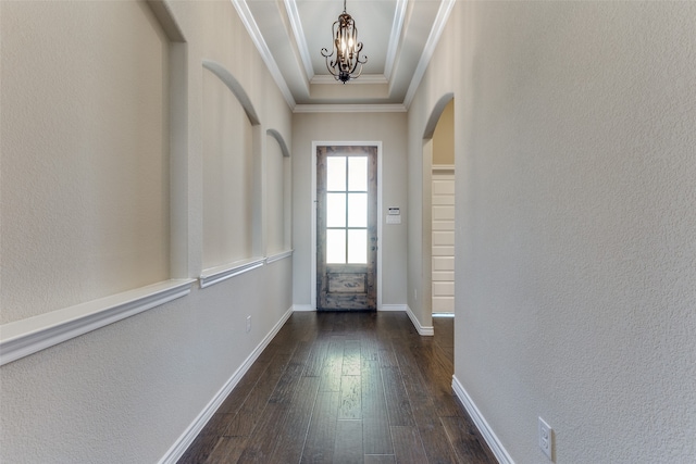 doorway to outside featuring a notable chandelier, dark wood-type flooring, ornamental molding, and a tray ceiling