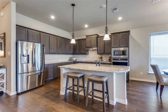 kitchen featuring dark hardwood / wood-style floors, hanging light fixtures, tasteful backsplash, an island with sink, and appliances with stainless steel finishes