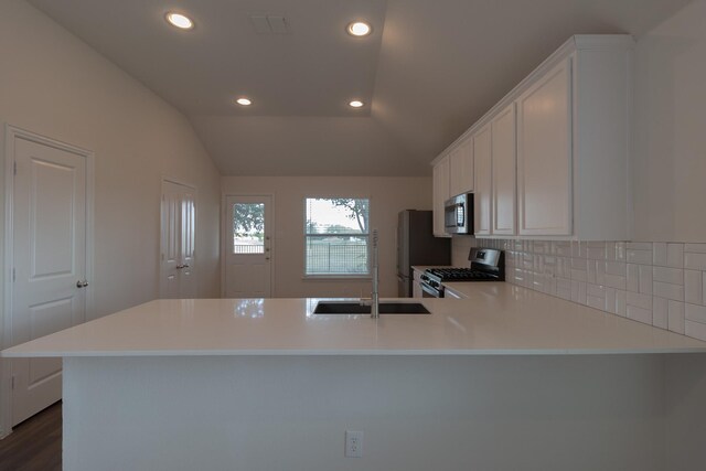 kitchen with appliances with stainless steel finishes, vaulted ceiling, dark wood-type flooring, backsplash, and kitchen peninsula