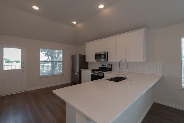 kitchen with stainless steel appliances, vaulted ceiling, kitchen peninsula, and white cabinets