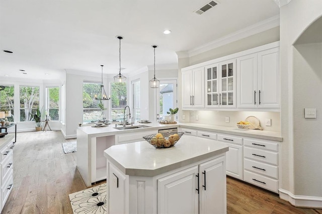 kitchen featuring crown molding, sink, light wood-type flooring, a kitchen island, and white cabinetry