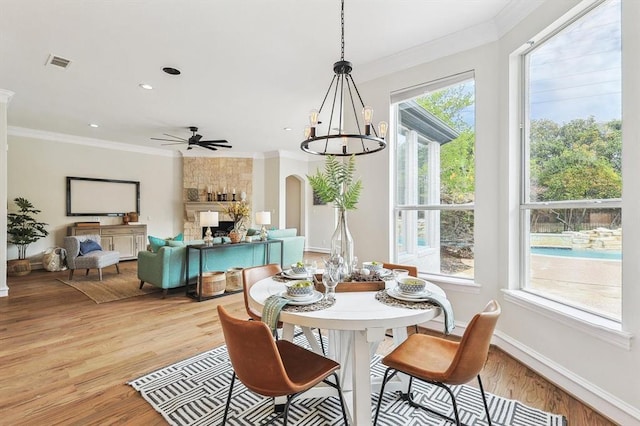 dining room with a fireplace, crown molding, light hardwood / wood-style flooring, and ceiling fan with notable chandelier