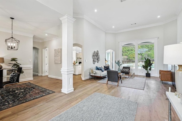 living room featuring ornate columns, crown molding, light hardwood / wood-style flooring, and an inviting chandelier