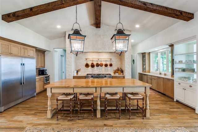 kitchen with high end appliances, vaulted ceiling with beams, hardwood / wood-style flooring, and a kitchen bar