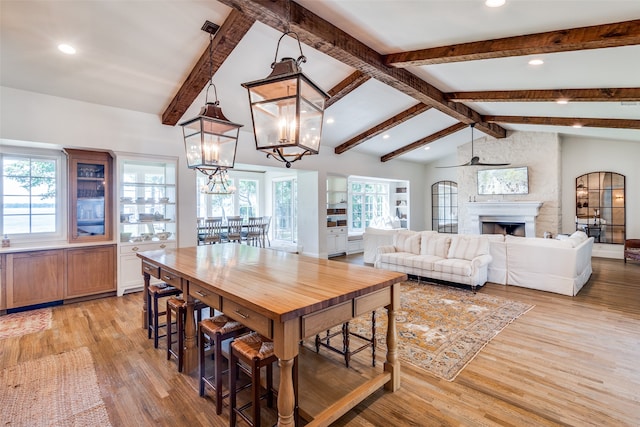 dining area with plenty of natural light, ceiling fan with notable chandelier, lofted ceiling with beams, and light hardwood / wood-style flooring