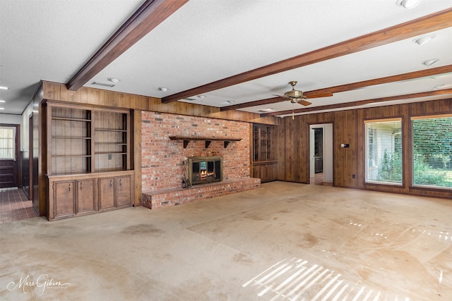 unfurnished living room with a brick fireplace, beamed ceiling, a textured ceiling, and wood walls