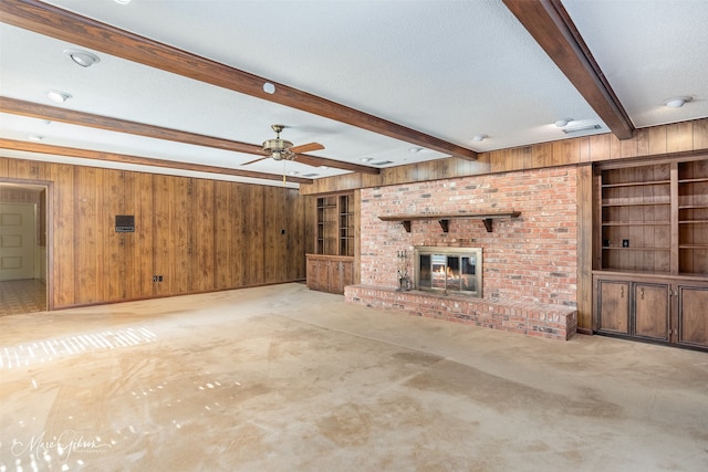 unfurnished living room with a brick fireplace, beam ceiling, a textured ceiling, and wood walls