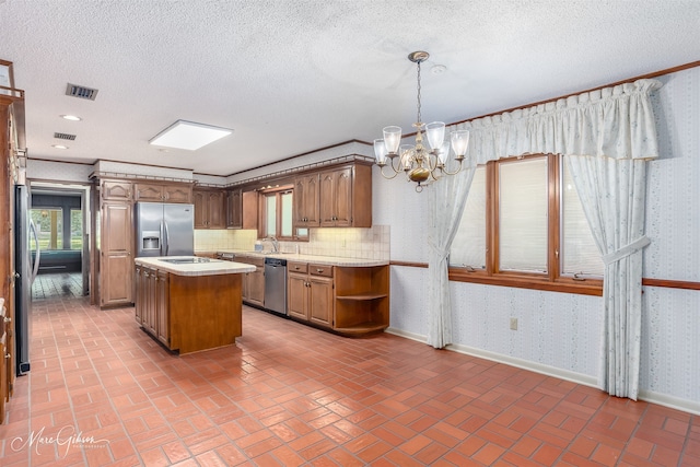 kitchen featuring a kitchen island, appliances with stainless steel finishes, pendant lighting, a notable chandelier, and a textured ceiling