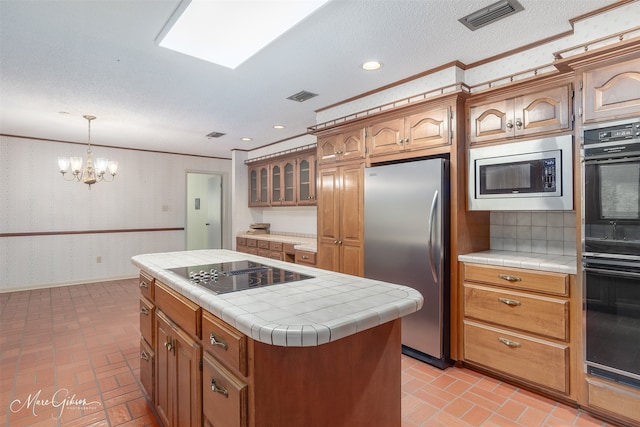 kitchen featuring a center island, a textured ceiling, hanging light fixtures, tile counters, and black appliances