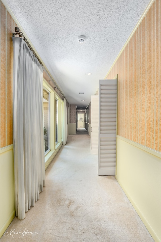 hall with light colored carpet and a textured ceiling