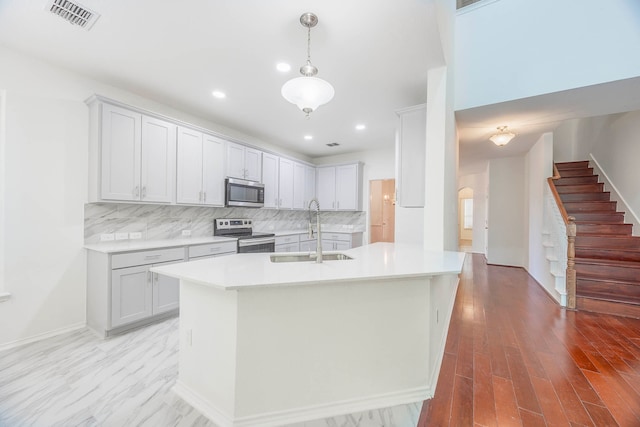 kitchen featuring light wood-type flooring, sink, hanging light fixtures, backsplash, and appliances with stainless steel finishes