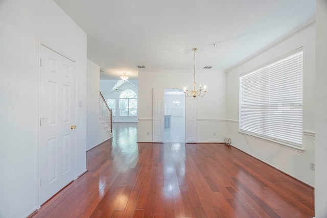 empty room with ornamental molding, an inviting chandelier, and dark wood-type flooring