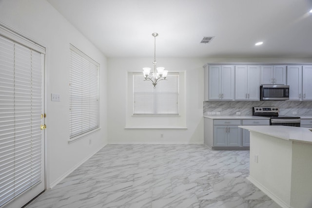 kitchen with gray cabinets, tasteful backsplash, hanging light fixtures, an inviting chandelier, and stainless steel appliances