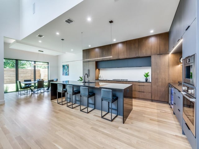 kitchen featuring light wood-type flooring, decorative light fixtures, oven, a breakfast bar area, and an island with sink