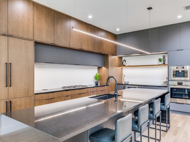 kitchen featuring sink, light hardwood / wood-style floors, a kitchen island, stainless steel gas stovetop, and a breakfast bar area