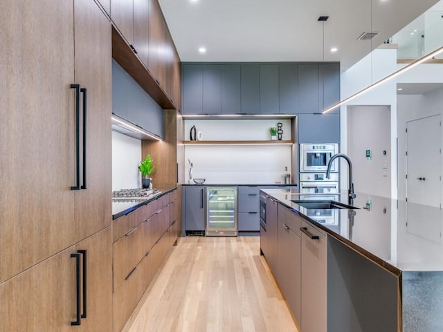 kitchen with sink, stainless steel appliances, beverage cooler, decorative light fixtures, and light wood-type flooring