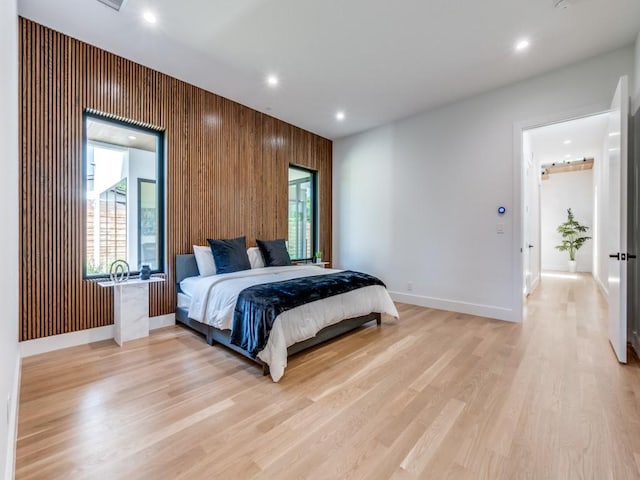 bedroom featuring light hardwood / wood-style flooring, multiple windows, and wooden walls