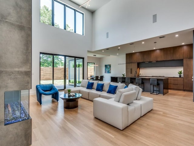 living room with light hardwood / wood-style flooring, a towering ceiling, and sink