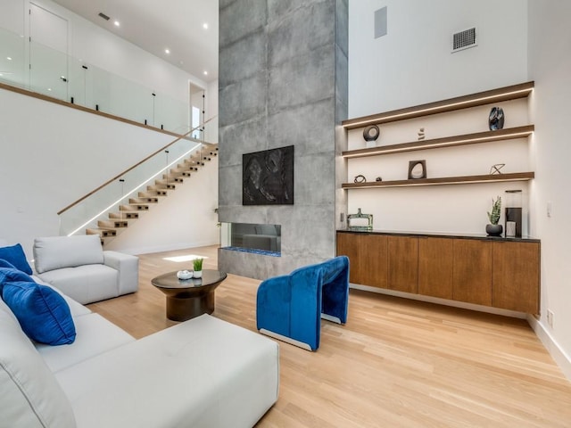 living room with a tiled fireplace, a towering ceiling, and light hardwood / wood-style floors