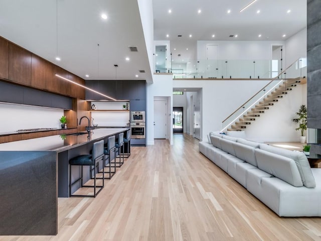 living room with light wood-type flooring, sink, and a towering ceiling