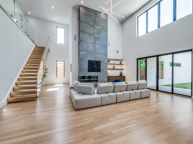 living room featuring a tiled fireplace, light hardwood / wood-style flooring, and a high ceiling