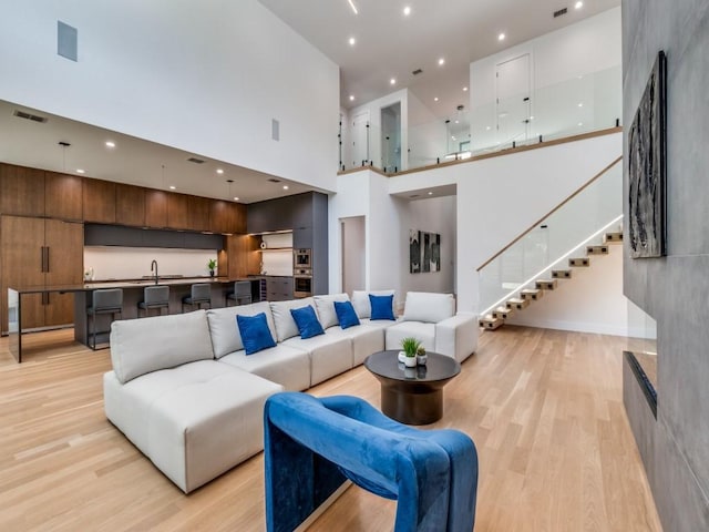 living room with a towering ceiling, light hardwood / wood-style flooring, and sink