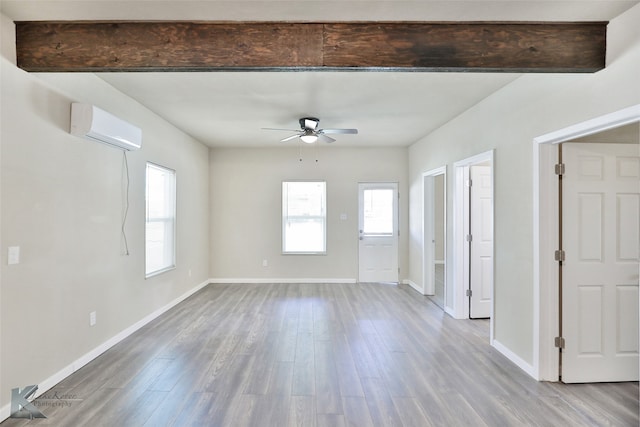 interior space with a wall mounted air conditioner, beamed ceiling, light wood-type flooring, and ceiling fan