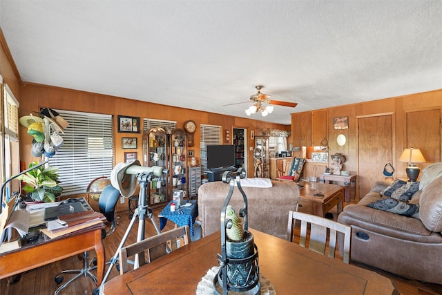 dining room with ceiling fan, a textured ceiling, and wood walls