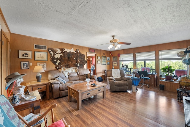 living room featuring ceiling fan, wooden walls, a textured ceiling, and hardwood / wood-style flooring