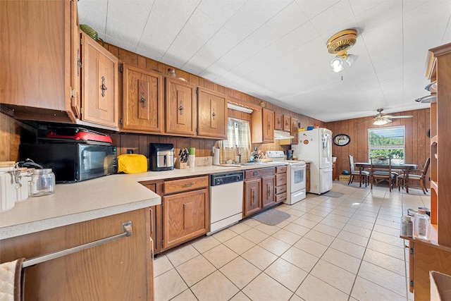 kitchen with white appliances, sink, wood walls, ceiling fan, and light tile patterned floors