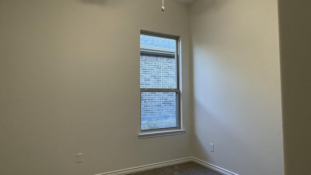 unfurnished room featuring baseboards, dark carpet, and a healthy amount of sunlight