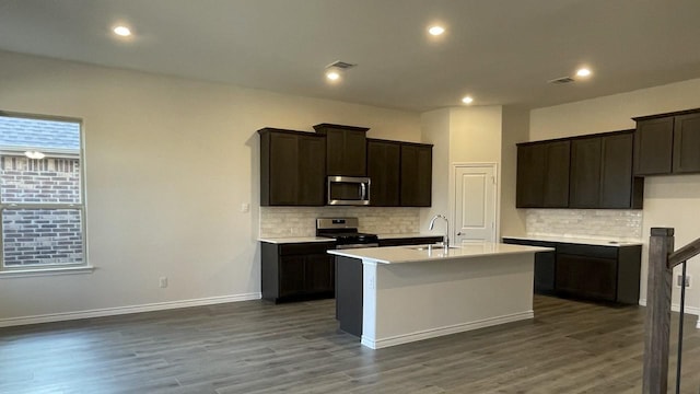 kitchen with dark wood-style floors, a center island with sink, stainless steel appliances, and a sink