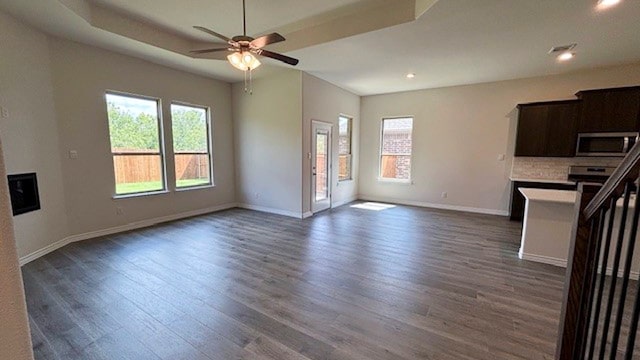 unfurnished living room with ceiling fan, a raised ceiling, and dark wood-type flooring