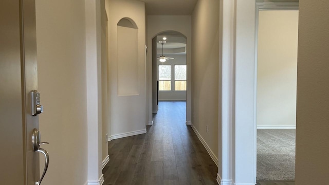 hall with baseboards, arched walkways, and dark wood-type flooring