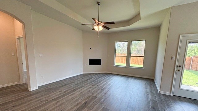 interior space featuring dark hardwood / wood-style flooring, a raised ceiling, a healthy amount of sunlight, and ceiling fan