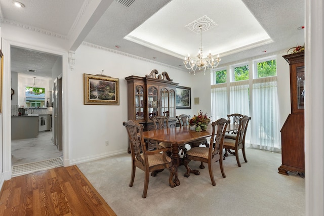 dining room with an inviting chandelier, a raised ceiling, light hardwood / wood-style flooring, a textured ceiling, and ornamental molding