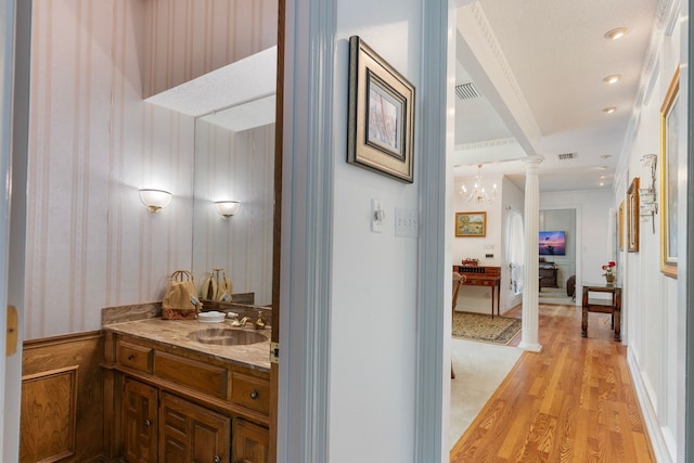 hallway featuring ornate columns, sink, a notable chandelier, light hardwood / wood-style floors, and ornamental molding