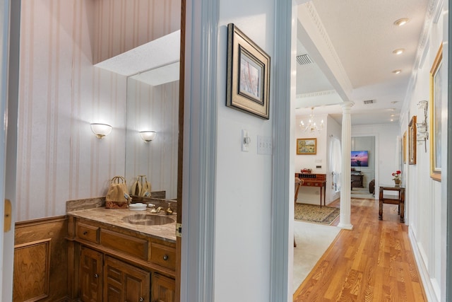 hall featuring visible vents, ornate columns, ornamental molding, a sink, and light wood-type flooring