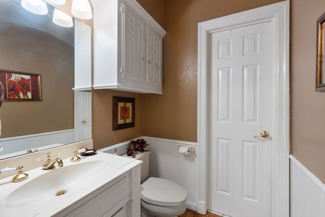 bathroom featuring vanity, toilet, and a wainscoted wall