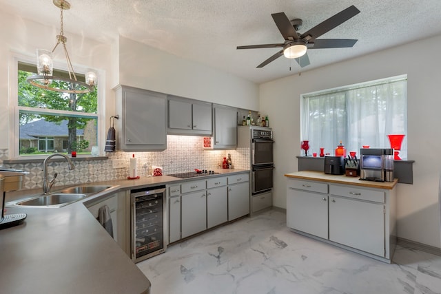 kitchen with sink, hanging light fixtures, wine cooler, black appliances, and ceiling fan with notable chandelier