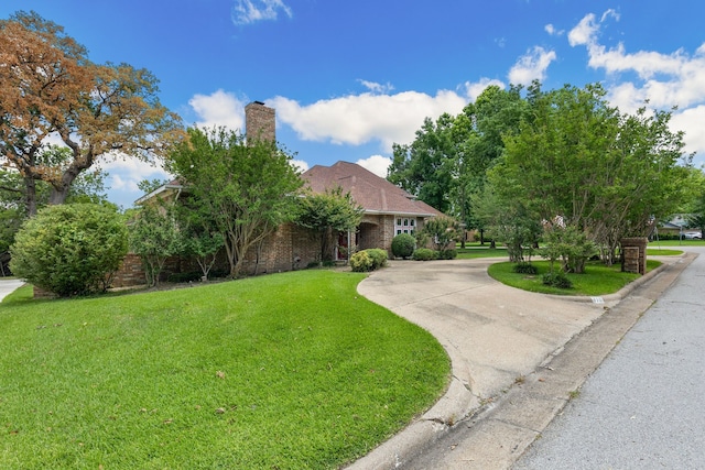 view of front of house featuring brick siding, curved driveway, a chimney, and a front lawn